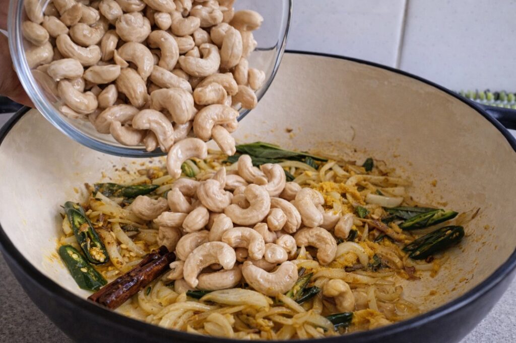 adding cashews to Sri Lankan cashew curry while cooking with onions and spices