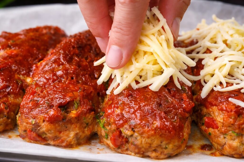 adding grated cheese on stuffed rolls with tomato sauce before baking