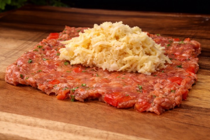 adding grated cheese to flattened minced meat for stuffed rolls filling