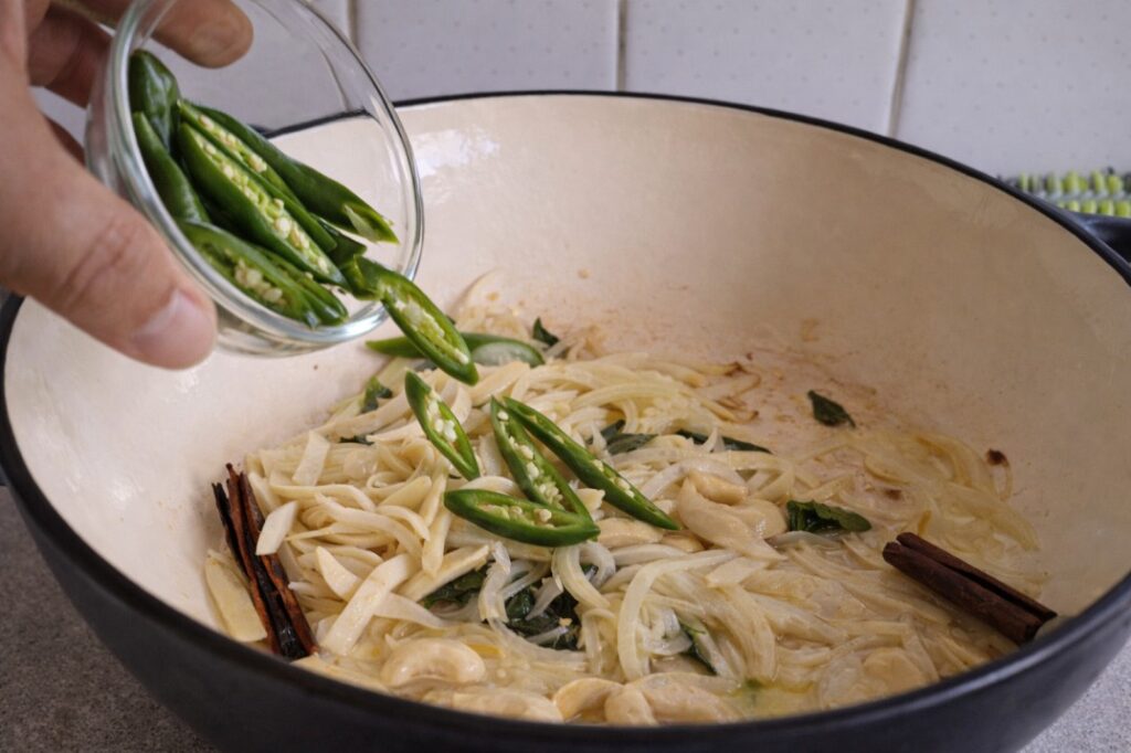 adding sliced green chilies to Sri Lankan cashew curry while cooking in a pan