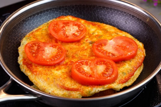 adding tomato slices on omelette while cooking in a pan