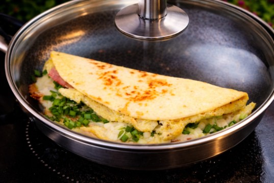 cooking omelette tortilla in a pan with lid covered to melt cheese