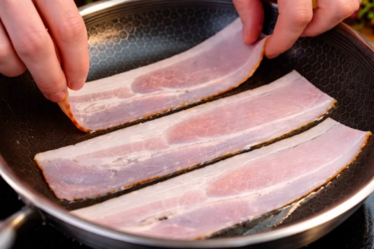frying bacon slices in a pan during breakfast preparation