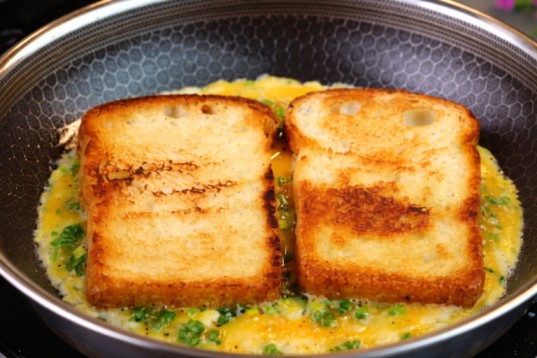 frying bread slices on egg mixture with herbs in a pan