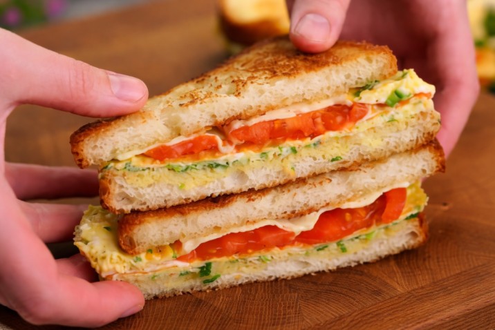 grilled sandwich with egg, cheese and tomato slices stacked on a wooden board