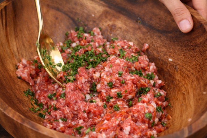 mixing minced meat with herbs and seasonings in a bowl for stuffed rolls