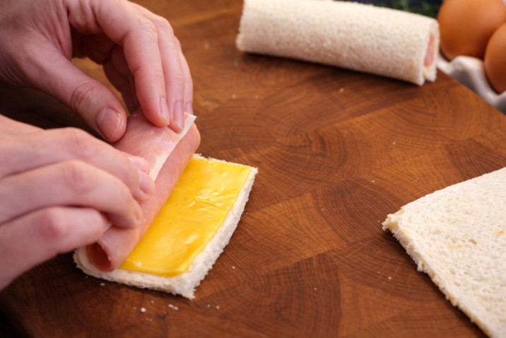 rolling bread slice with cheese and sausage to make stuffed bread rolls