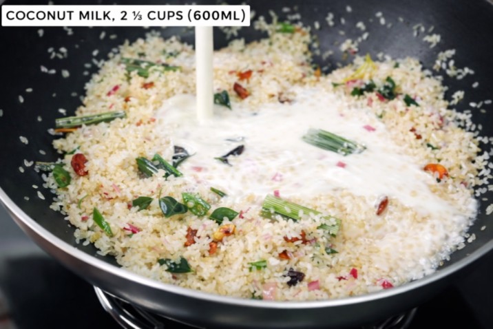 adding coconut milk to rice with spices while cooking in a pan