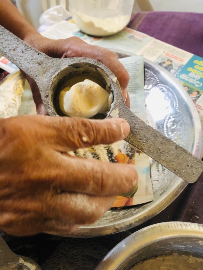 Pressing mani pittu dough by hand using a traditional string hopper maker